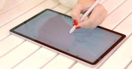 In love woman draws red heart shape on a digital tablet with a technological stylus for his partner....