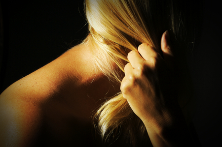 Abstract dramatically lit image of woman's shoulder, back, blond hair and hand gripping her hair.の写真素材