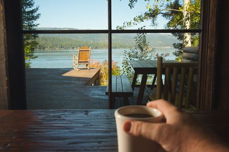 Man Holds Cup of Coffee while enjoying View Of Lakeの写真素材