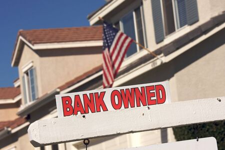 Bank Owned Real Estate Sign and House with American Flag in the Background.の写真素材