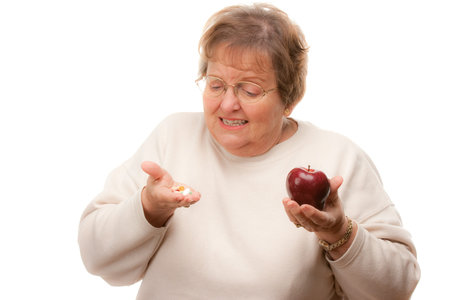 Confused Senior Woman Holding Apple and Vitamins Isolated on a White Background.の写真素材