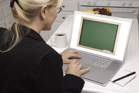 Woman In Kitchen Using Laptop with Blank Chalkboard ready for you own message. Screen can be easily...