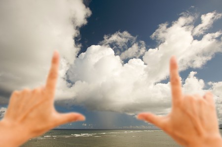 Hands Framing Dramatic Clouds over Tropical Shoreline on Kauai, Hawaiiの写真素材