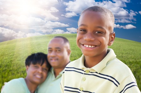 Handsome African American Boy with Proud Parents Standing Over Clouds, Sky and Arched Horizon of Grass Field.の写真素材