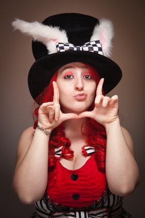 Attractive Red Haired Woman Wearing Bunny Ear Hat and Framing Her Face with her Hands on a Grey Background.の写真素材