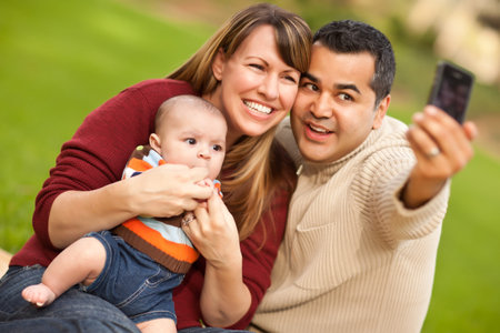 Happy Mixed Race Parents and Baby Boy Taking Self Portraits at the Park.の写真素材