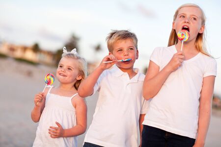 Cute Brother and Sisters Enjoying Their Lollipops at the Beach.の写真素材