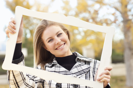 Pretty Young Woman Smiling in the Park on a Fall Day with Picture Frame.の写真素材