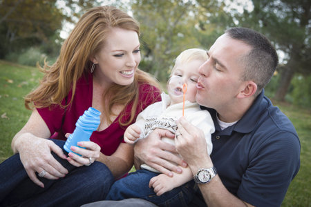 Attractive Young Parents Having Fun Blowing Bubbles with their Child Boy in the Park.
