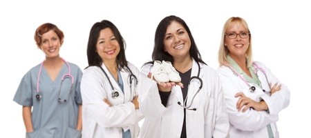 Attractive Hispanic Female Doctor or Nurse Holding Out Baby Shoes and Support Staff Behind Isolated on a White Background.の写真素材