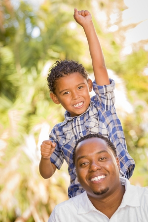 Happy Mixed Race Father and Son Cheering with Fist in the Air at the Park.の写真素材