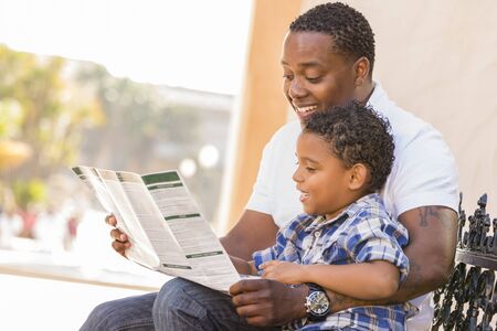 Happy African American Father and Mixed Race Son Having Fun Reading Park Brochure Outside.の写真素材