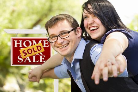 Happy Attractive Caucasian Couple in Front of Sold Real Estate Sign.の写真素材