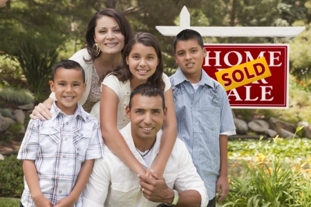 Happy Hispanic Family in Front of Sold Home for Sale Real Estate Sign.の写真素材