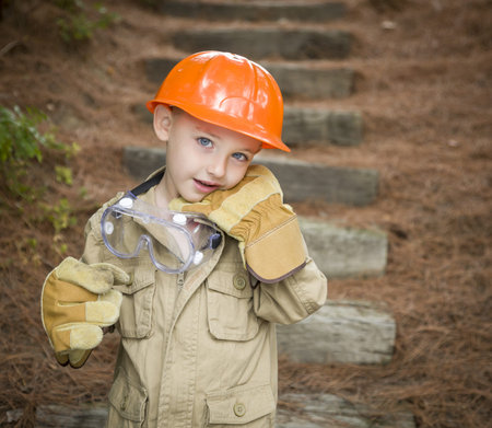 Happy Adorable Child Boy with Big Gloves, Hard Hat and Goggles Playing Handyman Outside.