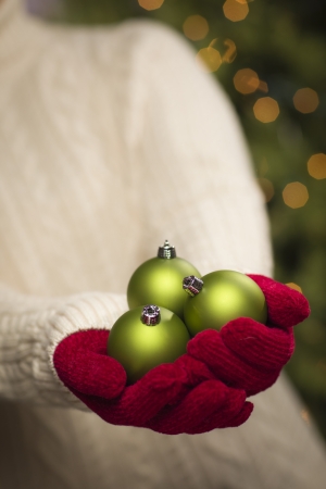 Woman Wearing A Sweater and Seasonal Red Mittens Holding Three Green Christmas Ornaments.の写真素材