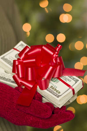 Woman Wearing Red Mittens and Green Sweater Holding Stacks of Hundreds of Dollars of Money with Red Ribbon.の写真素材
