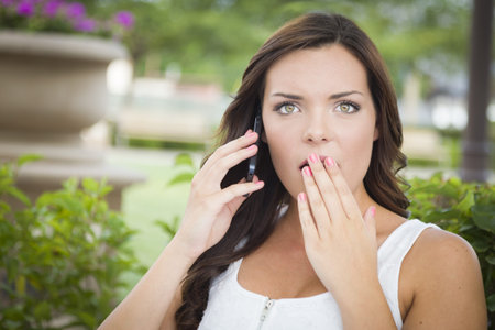 Shocked Young Adult Female Talking on Cell Phone Outdoors on Bench.