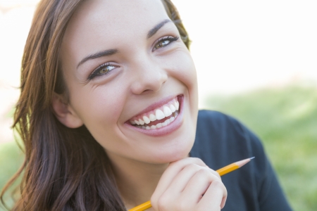Portrait of Pretty Young Female Student with Pencil on Campus Lawn.の写真素材