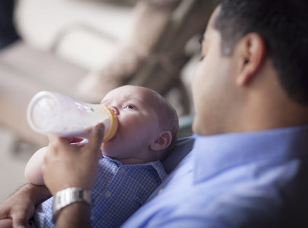 Happy Hispanic Father Bottle Feeding His Very Content Mixed Race Son.の写真素材
