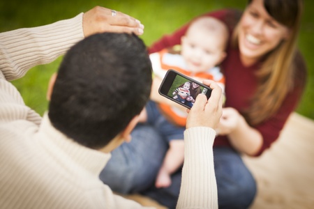 Happy Mixed Race Parents and Baby Boy Taking Self Portraits Outside at the Park.の写真素材