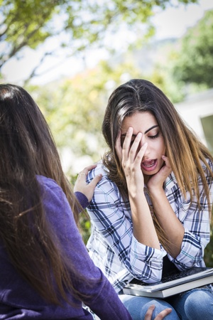 Sad or Stressed Young Mixed Race Girl Being Comforted By Her Friend Outside on Bench.の写真素材