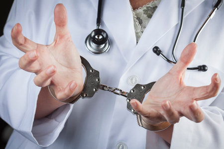 Female Doctor or Nurse In Handcuffs Wearing Lab Coat and Stethoscope.