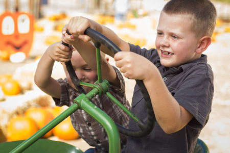 Adorable Young Boys Playing on an Old Tractor in a Rustic Outdoor Fall Setting.の写真素材