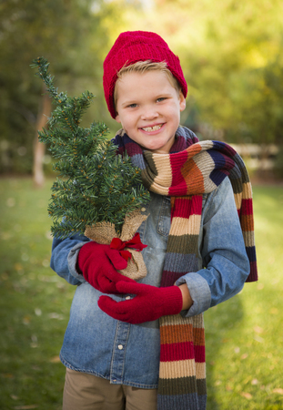 Handsome Young Boy Wearing Holiday Clothing Holding Small Christmas Tree Outside.の写真素材