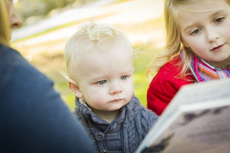 Mother Reading a Book to Her Two Adorable Blonde Children Wearing Winter Coats Outdoors.
の写真素材