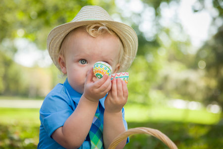 Cute Little Boy Wearing Hat Enjoying His Easter Eggs on Picnic Blanket Outside in the Park.