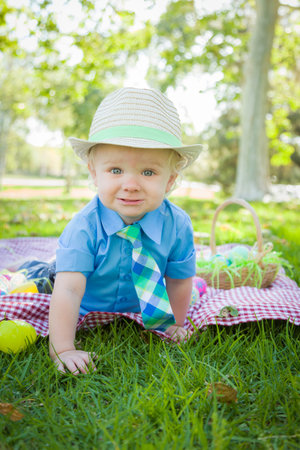 Cute Little Boy Smiles on Picnic Blanket With Easter Eggs Around Him.