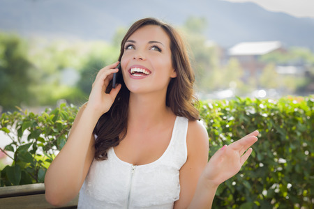 Attractive Young Adult Female Talking on Cell Phone Outdoors on Bench.の写真素材