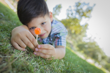Handsome Young Boy Enjoying His Lollipop Outdoors on the Grass.の写真素材