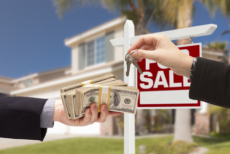 Agent Handing Over Keys as Buyer is Handing Over Cash for House with Home and For Sale Real Estate Sign Behind. Agent Handing Over Keys as Buyer is Handing Over Cash for House with Home and For Sale Real Estate Sign Behind.