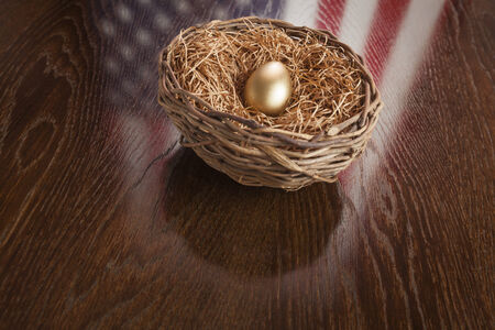 Golden Egg in Nest with American Flag Reflection on Wooden Table.の写真素材