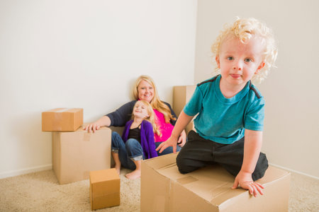 Playful Young Family In Empty Room Playing With Moving Boxes.