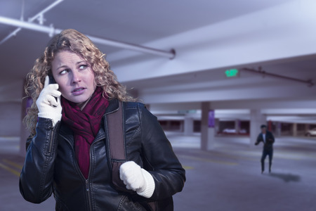 Frightened Young Woman On Cell Phone As Dark Man Lurks in Parking Structure.の写真素材