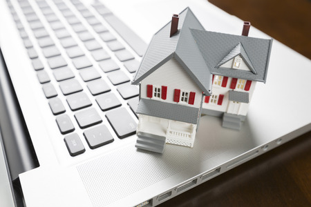 Miniature House And Laptop Computer Resting on Desktop.の写真素材