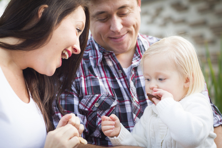 Adorable Little Girl Eating a Cookie with Mommy and Daddy Outside.の写真素材
