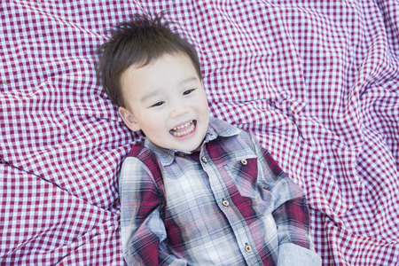 Cute Young Mixed Race Boy Laughing On Picnic Blanket Outside.の写真素材