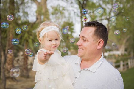 Affectionate Father Holding Cute Baby Girl Enjoying Bubbles Outside at the Park.の写真素材