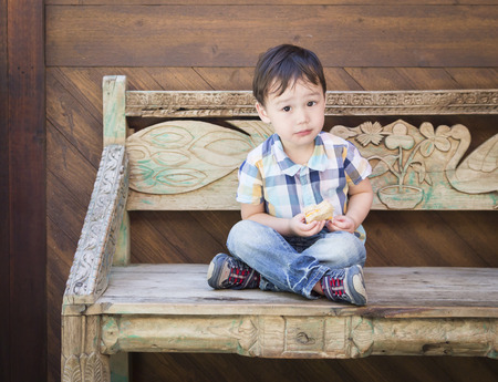 Cute Relaxed Mixed Race Boy Sitting on Bench Eating His Sandwich.の写真素材