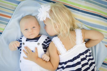 Cute Little Sister Laying Next to Her Baby Brother on Blanket.の写真素材