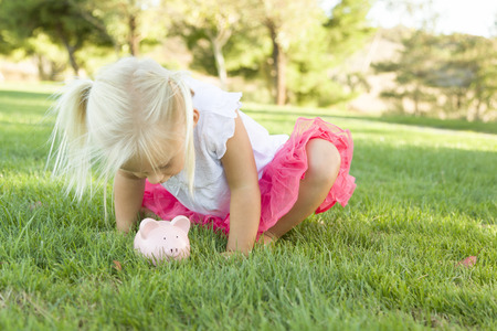 Cute Little Girl Having Fun with Her Piggy Bank Outside on the Grass.の写真素材
