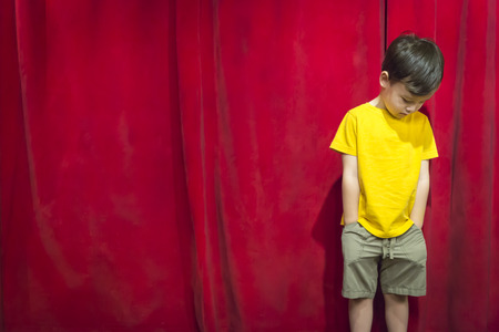 Sad Pouting Mixed Race Boy Standing In Front of Red Curtain.の写真素材