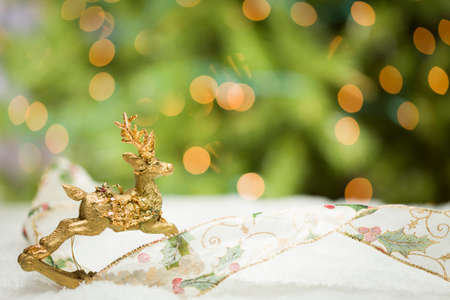 Decorative Christmas Reindeer Ornament and Ribbon on Snow with Tree and Lights Background.の写真素材