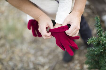 Caring Mother Putting Red Mittens On Child Near Small Christmas Tree Abstract.の写真素材