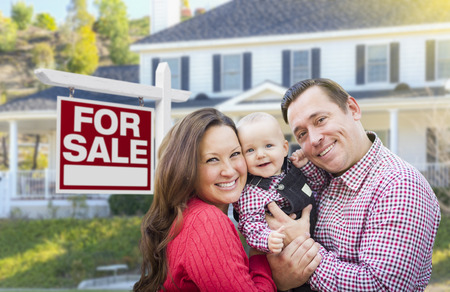 Happy Young Family In Front of For Sale Real Estate Sign and House.の写真素材