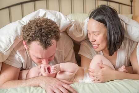 Mixed Race Chinese and Caucasian Baby Boy Laying In Bed with His Father and Mother.の写真素材